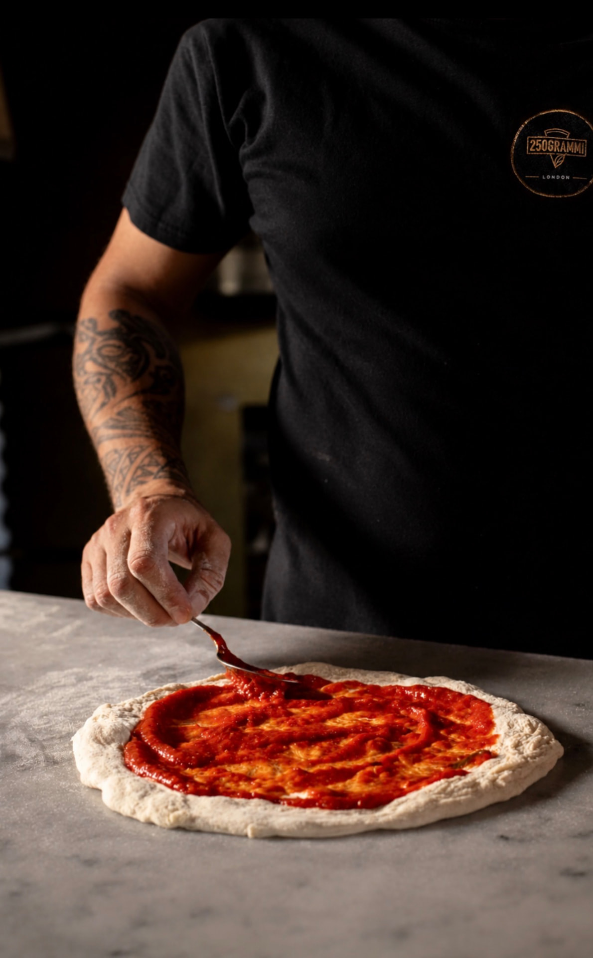 A pizzaiolo spreading tomato over hand-shaped dough